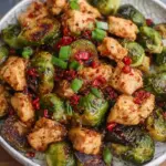 A bowl of crispy air-fried chicken cubes and halved Brussels sprouts glazed in sweet chili sauce with sesame seeds.