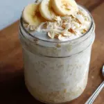 Two mason jars filled with creamy banana cream pie overnight oats topped with fresh banana slices.