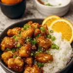 Golden brown glazed healthy orange chicken cubes garnished with green onions in a skillet