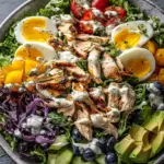 A row of four meal prep containers filled with grilled chicken, quinoa, kale, and fresh vegetables.