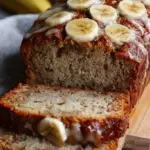 A golden loaf of high protein banana bread sliced on a wooden board