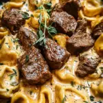 A skillet of golden seared steak cubes and cheese tortellini in a creamy garlic sauce with fresh spinach.
