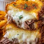 Golden brown French dip grilled cheese sandwich sliced diagonally with a side of savory beef au jus.