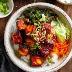 Crispy cubed tofu coated in a glossy red gochujang glaze with green onions and sesame seeds.