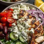A vibrant Greek chicken bowl with grilled chicken, cucumber, tomatoes, feta, and tzatziki over brown rice.