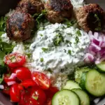 A colorful Greek Meatball Bowl with lemon rice, cherry tomatoes, olives, and creamy tzatziki sauce.