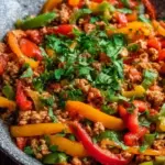 A colorful skillet filled with browned ground turkey and sliced red, yellow, and green bell peppers.