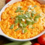 A bubbling dish of healthy buffalo chicken dip topped with melted mozzarella and fresh green onions.