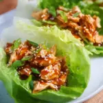 A plate of fresh butter lettuce cups filled with glazed teriyaki ground chicken and topped with sesame seeds.