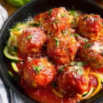 A tray of golden brown turkey ricotta meatballs on parchment paper with fresh herbs.