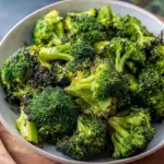 Crispy air fried broccoli florets coated in nutritional yeast and almond flour in a white bowl.