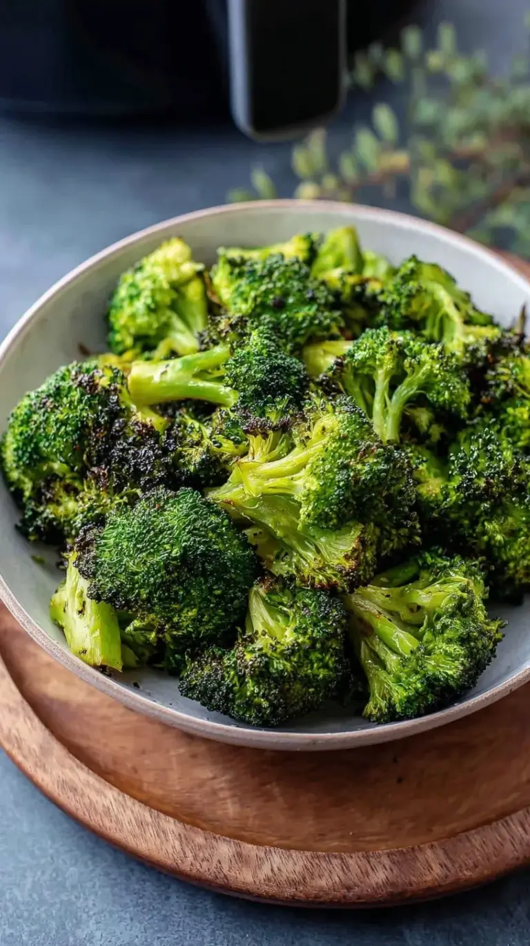 Crispy air fried broccoli florets coated in nutritional yeast and almond flour in a white bowl.