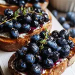Two slices of sprouted grain toast topped with creamy whipped cottage cheese and balsamic macerated blueberries.