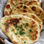Golden brown garlic naan bread brushed with fresh cilantro butter on a wooden board.