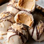 A tray of frozen peanut butter yogurt bites topped with mini dark chocolate chips on parchment paper.