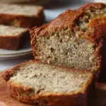 A sliced loaf of golden brown high protein gluten free banana bread on a wire cooling rack.