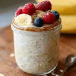 A glass jar filled with creamy overnight oats topped with fresh berries and nuts.