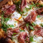 A golden brown pizza topped with creamy burrata cheese, salty prosciutto, fresh arugula, and a drizzle of honey and balsamic glaze.