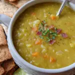A steaming bowl of green split pea soup with diced ham and carrots