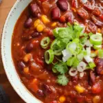 A steaming bowl of thick three bean vegetarian chili topped with fresh herbs