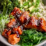 A vibrant bowl with glazed salmon, jasmine rice, sliced avocado, and fresh cucumber.