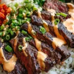 A vibrant bowl of seared steak, white rice, kimchi, and carrots with a creamy sauce drizzle.