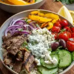 A vibrant Mediterranean gyro bowl with seasoned meat, fresh tomatoes, cucumbers, and creamy tzatziki sauce over rice.
