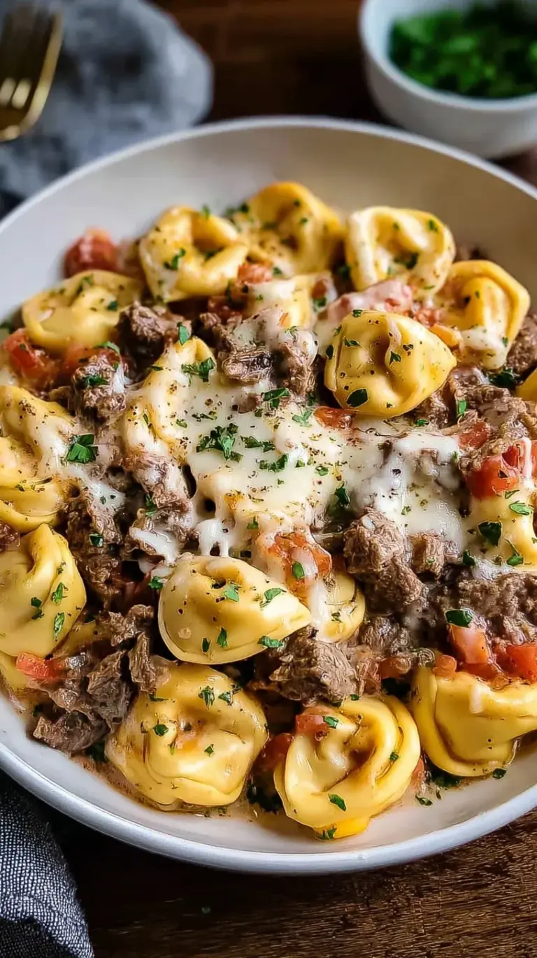 A skillet of creamy Philly cheesesteak tortellini pasta with sliced steak and peppers.