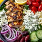 A vibrant Greek chicken bowl with quinoa, cucumbers, tomatoes, and feta cheese
