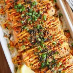 A creamy salmon sushi bake in a ceramic dish topped with green onions and unagi sauce