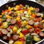 A colorful skillet filled with browned smoked sausage, red and green bell peppers, onions, and zucchini.