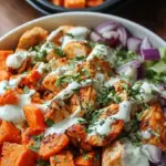 A sheet pan filled with roasted buffalo chicken cubes and golden sweet potato cubes garnished with green onions.
