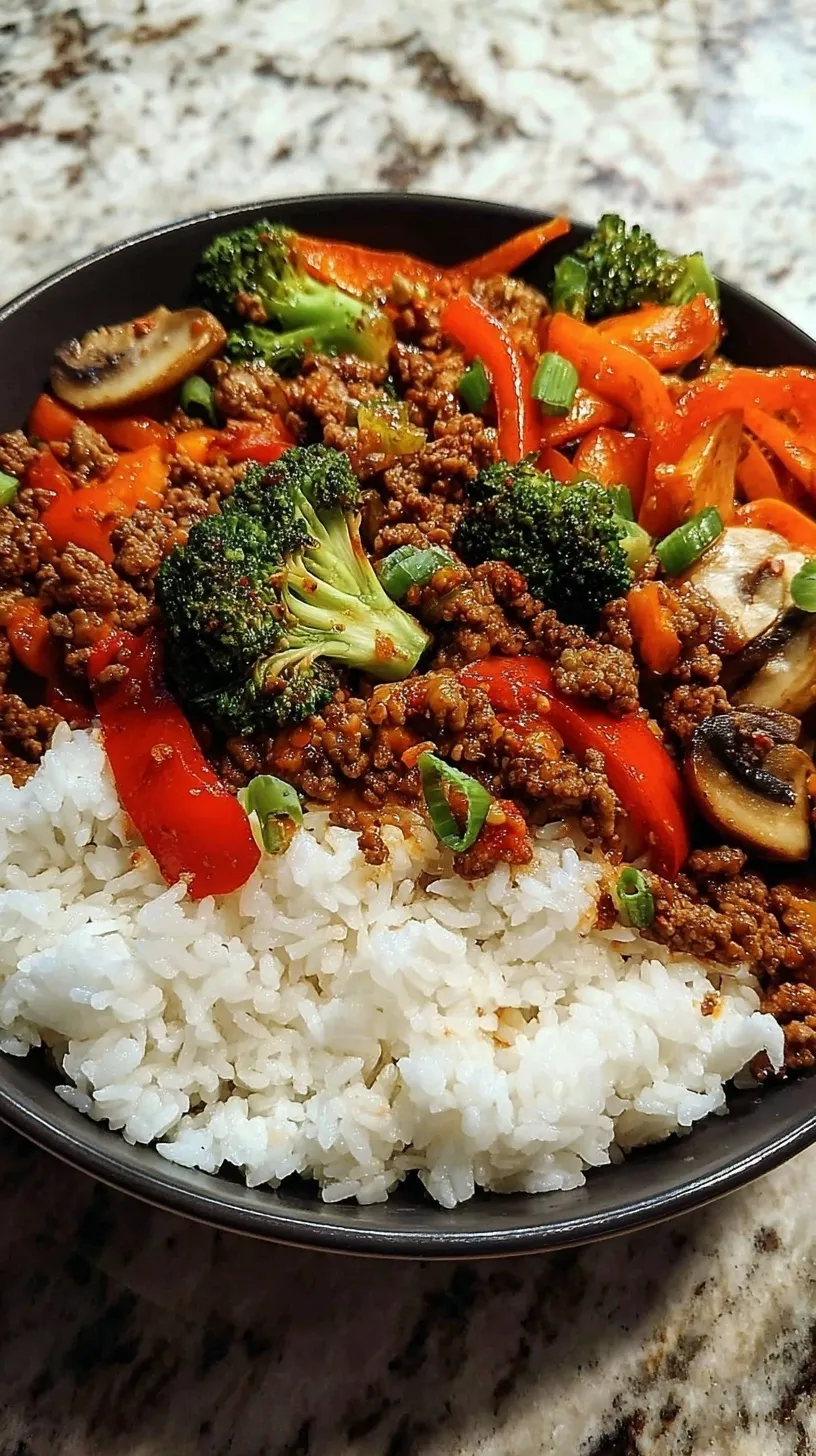 A colorful spicy ground beef stir fry bowl with steamed broccoli, red peppers, and fluffy rice.