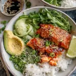 A vibrant bowl of seared spicy salmon cubes, sliced avocado, and cucumber over fluffy coconut rice.